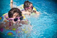 kids swimming and playing in a pool. is chlorine bad for your skin